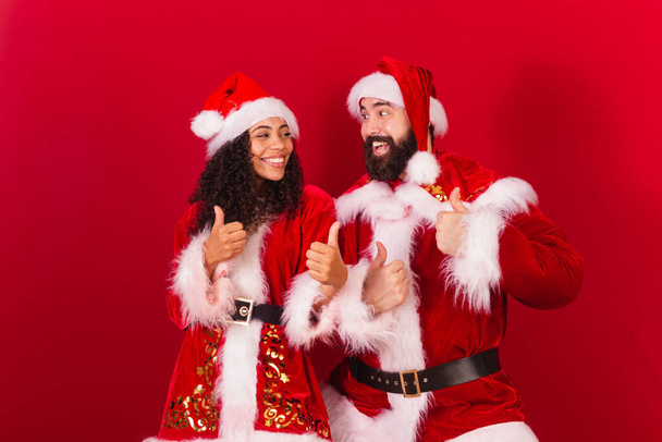 ブラジル人の夫婦はクリスマスにサンタ・クラスにミイラの服を着て。黒人女性や白人男性の手と同じように. - 写真・画像