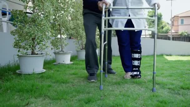 bejaardenpaar helpen om te leren lopen met een wandelaar in hun voortuin. familierelatie, koppel, zorg, gezondheid, ziekte - Video