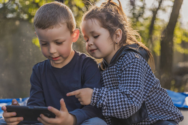 portrait of children who sit on a trampoline and look at the phone - Photo, Image