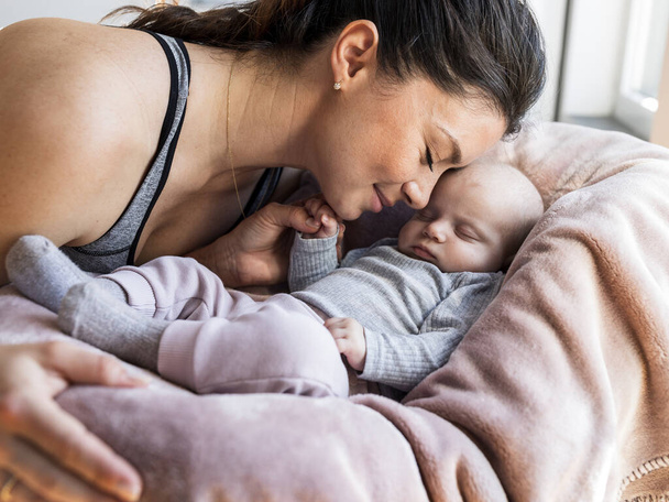 Mama przytula się do nowonarodzonego dziecka, które śpi i trzyma palec mamy małą ręką. Pojęcie miłości macierzyńskiej i opieki - Zdjęcie, obraz