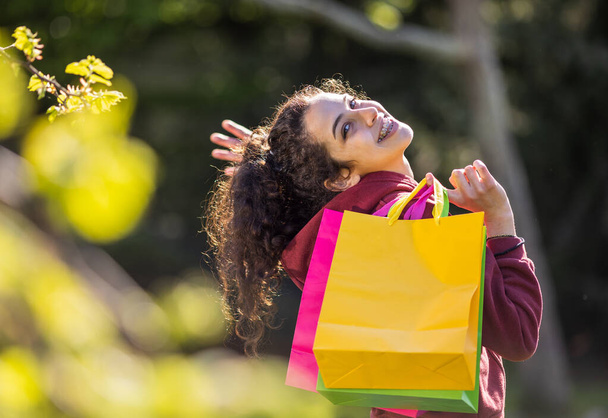Emocionado adolescente sosteniendo bolsas de compras en el parque y mirando por encima del hombro - Foto, Imagen