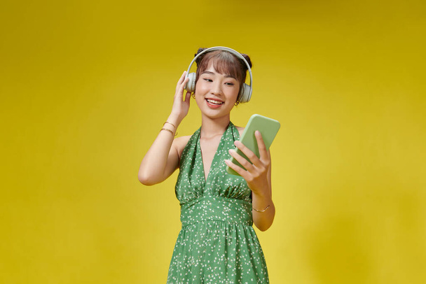 携帯電話から音楽を聴いてヘッドフォンを身に着けている幸せなアジアの女の子リラックス - 写真・画像