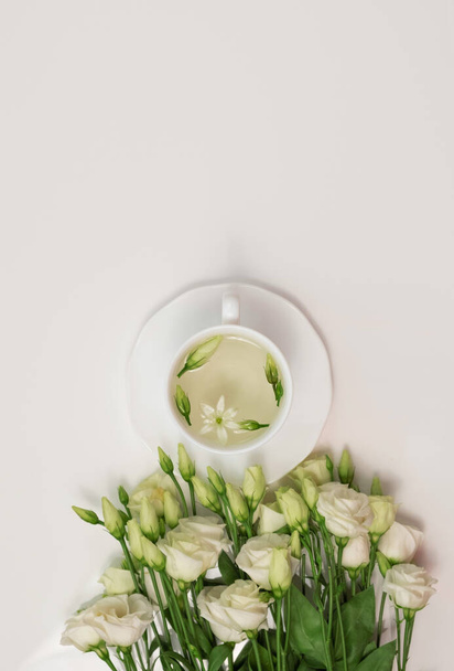 Квітковий чай. Біла чашка з запашним трав'яним чаєм та квітами Eustoma Lisianthus. Час чаю. Розслабляючись з трав'яним чаєм, білий фон, вид зверху, вертикальний
 - Фото, зображення