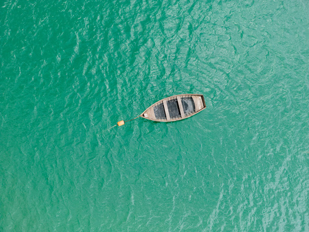 Ein atemberaubender Blick von oben auf einen ruhigen blau-grünen See mit einem Holzboot, das sanft auf seiner Oberfläche schwebt. - Foto, Bild