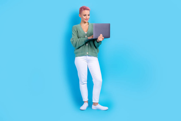 Full body photo of young satisfied business blogger pink hair woman writing own book using her laptop isolated on blue color background. - 写真・画像
