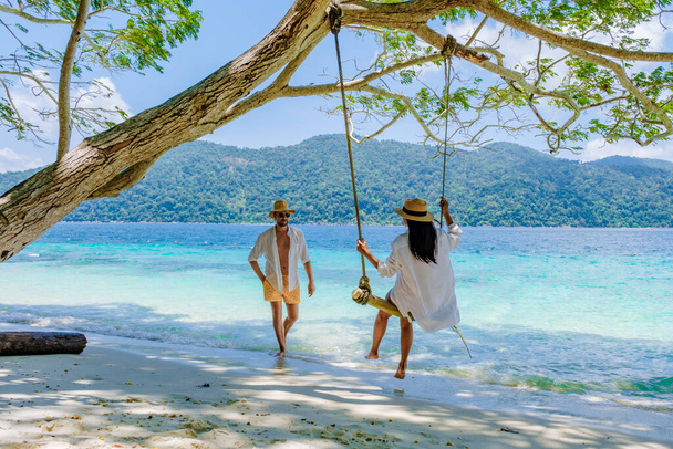 南タイのコラー島のビーチでロープスイングで遊ぶカップル、タルタオ国立公園、コラウィ、タンボンコTarutaoでターコイズブルーの海と熱帯の白い砂浜 - 写真・画像