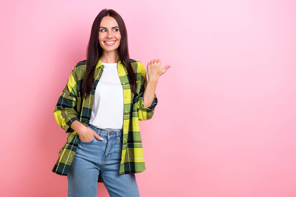 Photo of tricky shiny woman dressed plaid shirt looking showing thumb empty space isolated pink color background. - Foto, afbeelding