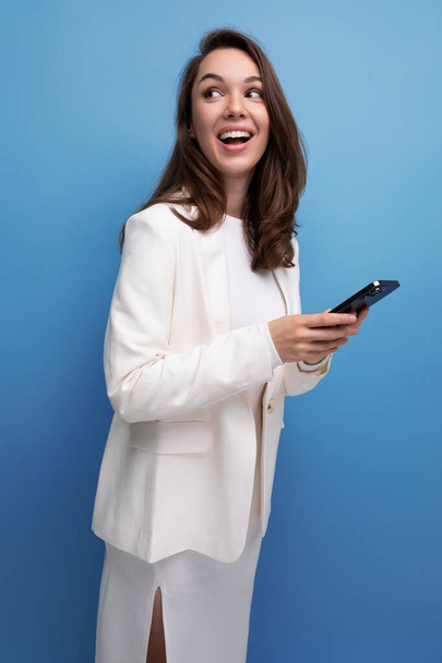 Siyah, uzun saçlı, beyaz elbiseli bir kadın elinde akıllı bir telefonla internette sohbet ediyor.. - Fotoğraf, Görsel