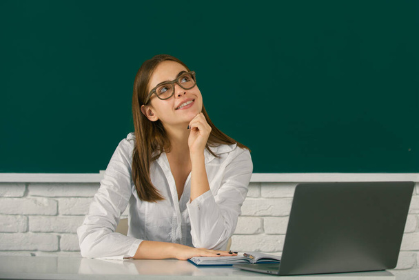 Portrait of dreaming young college student in classroom on blackboard background, copy space - Photo, image