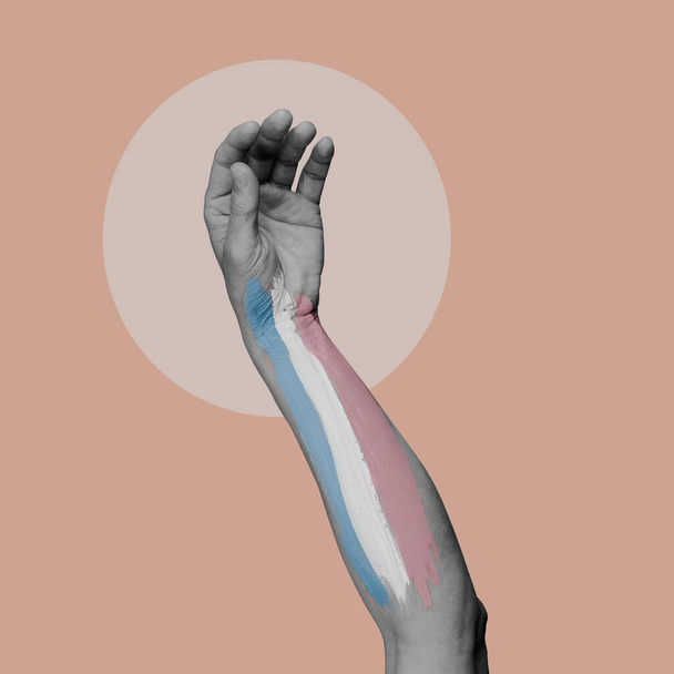 el brazo de una persona en blanco y negro con una bandera de orgullo transgénero pintada en ella, sobre un fondo rosa - Foto, imagen