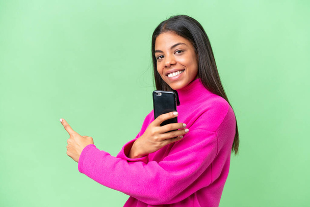 Nuori Afrikkalainen Amerikkalainen nainen yli eristetty tausta matkapuhelimella ja osoittaa taaksepäin - Valokuva, kuva