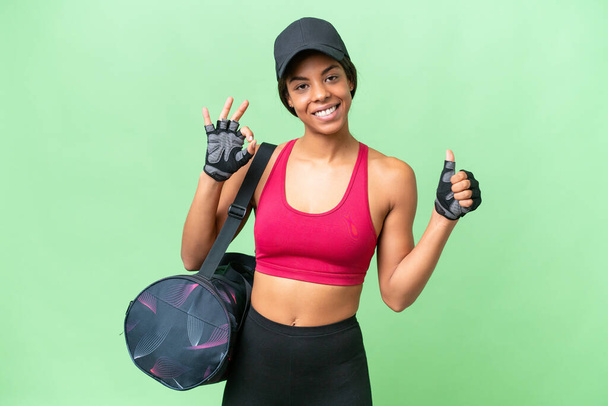 Jonge sport Afrikaanse Amerikaanse vrouw met sporttas over geïsoleerde achtergrond tonen ok teken en duim omhoog gebaar - Foto, afbeelding