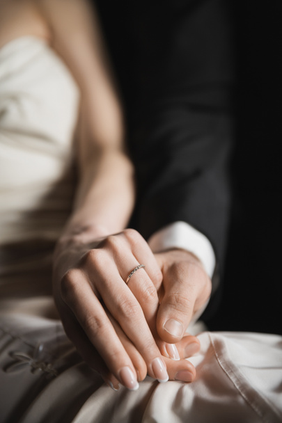 ostříhaný pohled na šťastné novomanžele, nevěstu s elegantním a luxusním snubním prstenem na prstu a ženicha držící se za ruce po svatbě v hotelovém pokoji  - Fotografie, Obrázek