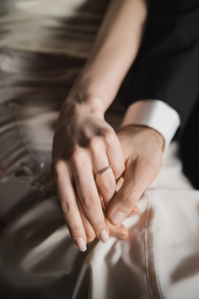 ostříhaný pohled na novomanžele, nevěstu s elegantním a luxusním snubním prstenem na prstu a ženicha v obleku držící se za ruce po svatbě v hotelovém pokoji  - Fotografie, Obrázek