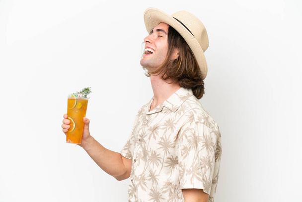 Young handsome man holding a cocktail isolated on white background laughing in lateral position - Foto, immagini