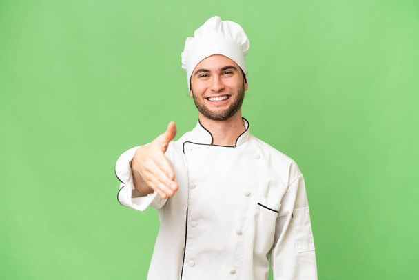 Junge gut aussehende Koch Mann über isolierten Hintergrund schüttelt Hände für den Abschluss eines guten Geschäfts - Foto, Bild