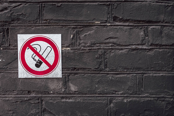 Black brick wall with no smoking sign. No smoking. Bad habit. Nicotine addiction. Prohibition sign. Brick background. Black paint. Rough surface. - Photo, Image