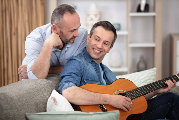 gay couple with guitar sitting on sofa at home - Foto, Imagem