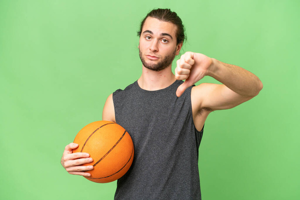Young basketball player man over isolated background showing thumb down with negative expression - Photo, image