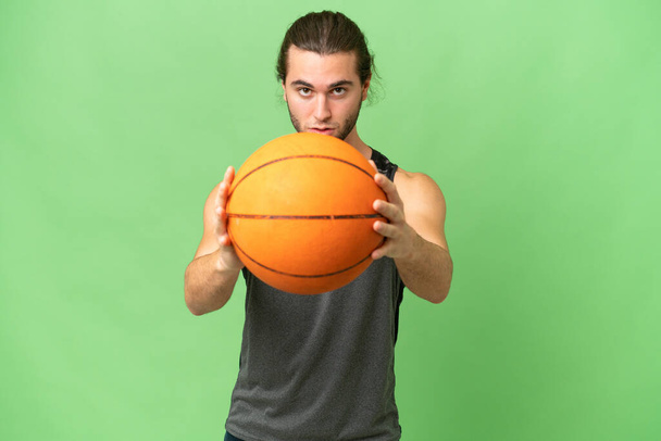 Young handsome man isolated on green chroma background playing basketball - Photo, Image