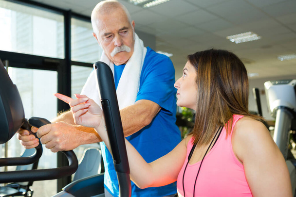 fitness instructor advising senior man using equipment - Fotó, kép