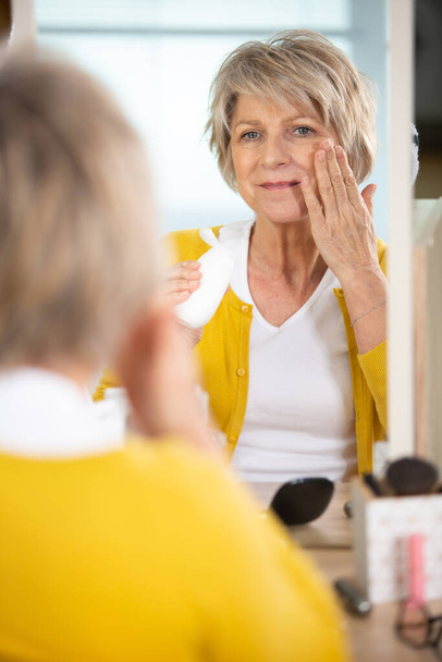 lady in her fifties applies skincare product to her face - Foto, Imagem