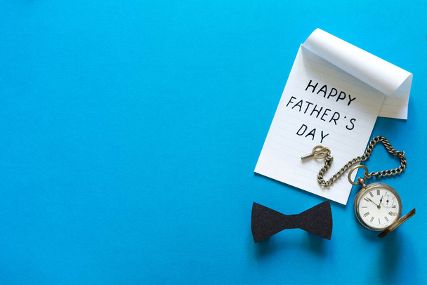 Happy Fathers Day Concept. Black stylish paper bow tie and vintage pocket watch with key chain on blue background. Blank greeting card, invitation mockup. Flat lay, top view - Foto, imagen