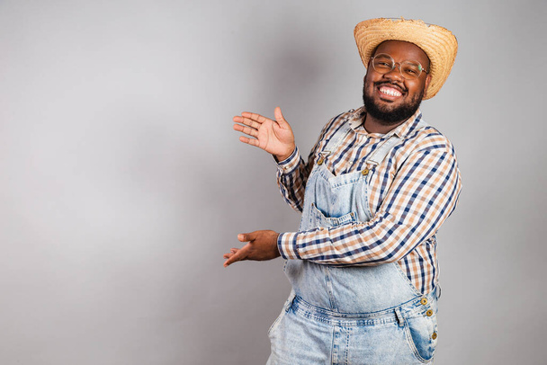 brazilian black man wearing country clothes from festa junina,festa de so joo. Presenting something to the right. Announcement. - Zdjęcie, obraz