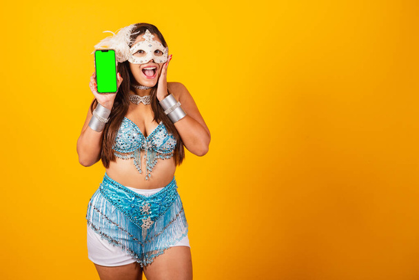Beautiful Brazilian woman in blue and white carnival clothes. holding smartphone with green screen. - 写真・画像