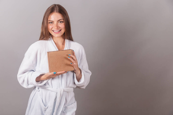 Brazilian blonde woman showing wonderful hair. dressed in a robe. holding small cardboard boxes with cosmetics. - Fotoğraf, Görsel