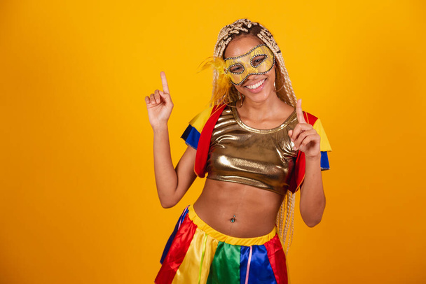 beautiful black Brazilian woman, dressed in carnival clothes, mask. yellow background. dancing, celebrating. - Photo, Image