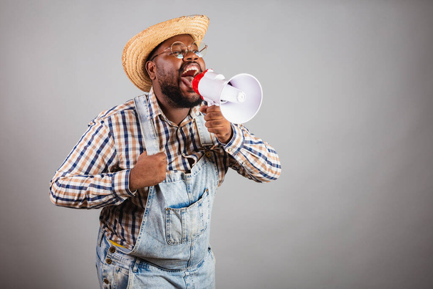 brazilian black man wearing country clothes from festa junina,festa de so joo. arrai, using megaphone shouting promotion, announcing advertisement, discount. - Fotografie, Obrázek