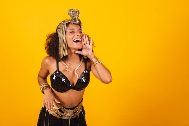 Beautiful black Brazilian woman, in Cleopatra carnival clothes, shouting promotion, advertising. - Фото, изображение