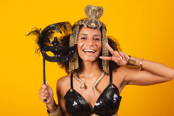Beautiful black Brazilian woman, in Cleopatra carnival clothes, holding carnival mask, taking close-up portrait. - Photo, Image