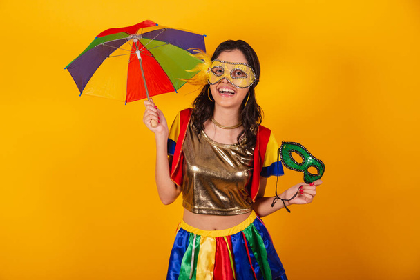 beautiful brazilian woman in carnival clothes, with frevo clothes, and colorful umbrella and mask. smiling. - Foto, Bild