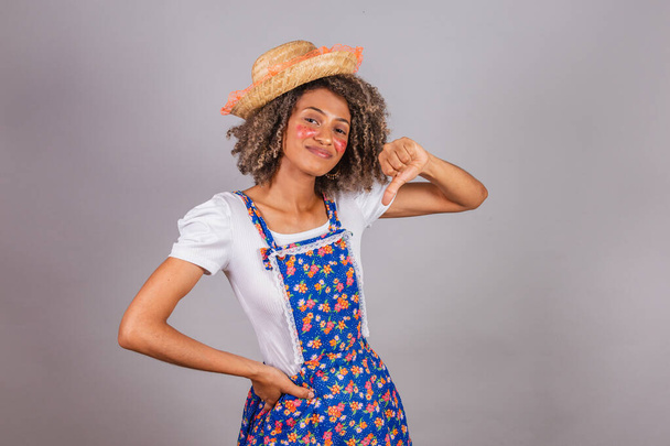 Young black Brazilian woman, with country clothes, dressed for Festa Junina. Saint John's festival. Thumb down, negative, frustrated, disapproving. - Foto, imagen