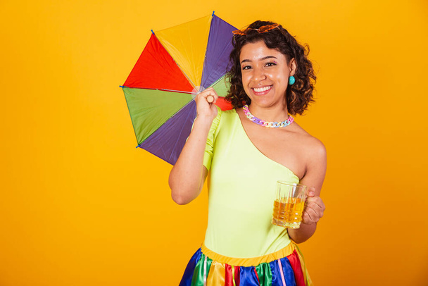 beautiful afro american brazilian woman, with carnival clothes, holding glass of beer and colorful parasol. - Фото, зображення