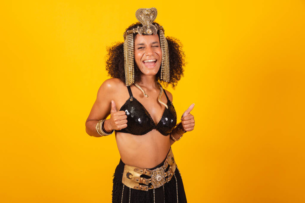 Beautiful black Brazilian woman, in Cleopatra carnival clothes, thumb raised, positive - 写真・画像