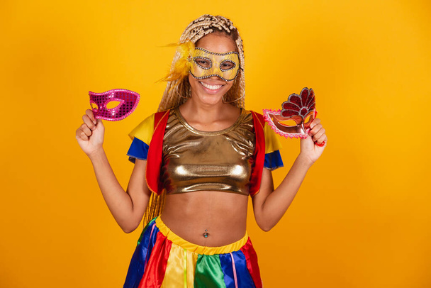 beautiful black Brazilian woman, dressed in carnival clothes, mask. yellow background. holding carnival masks. - Фото, зображення