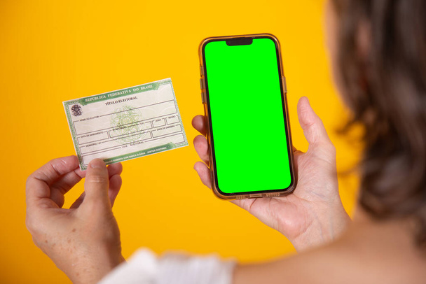 hand holding Brazilian voter registration card and smartphone with green screen - Photo, image