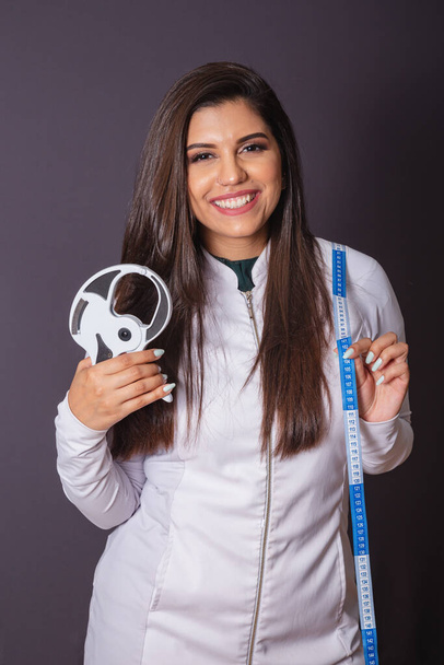 Horizontal photo. brazilian woman with medical coat, nutritionist. adipometer and measuring tape. slimming. - 写真・画像