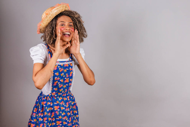 Young black Brazilian woman, with country clothes, dressed for Festa Junina. Saint John's festival. shouting promotion, advertising. - Foto, afbeelding