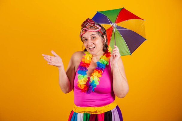 Adult woman in carnival clothes, smiling at camera with holding colorful parasol. saying welcome. - Foto, Imagem