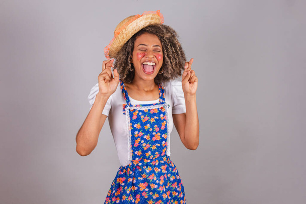 Young black Brazilian woman, with country clothes, dressed for Festa Junina. Saint John's festival. Fingers crossed, lucky sign, cheering hard. - Photo, Image