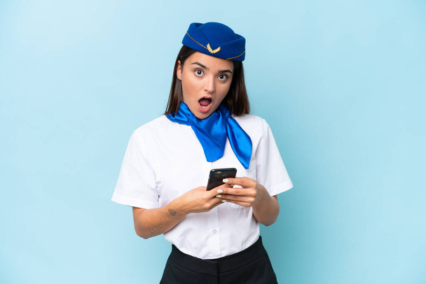 stewardessa samolot kaukaska kobieta izolowane na niebieskim tle zaskoczony i wysyłanie wiadomości - Zdjęcie, obraz