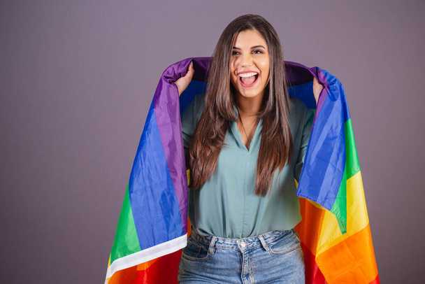Horizontal photo. Beautiful Brazilian woman, with casual clothes, Jeans and green shirt. holding lgbt flag. - 写真・画像