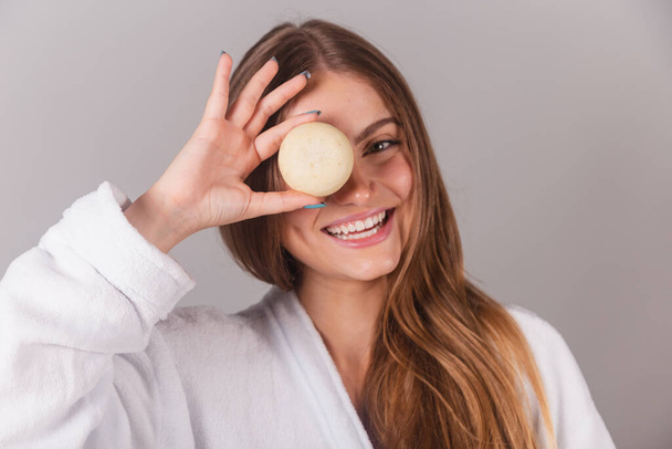 beautiful brazilian woman dressed in bathrobe, holding soap for skin care. close-up photo. - 写真・画像