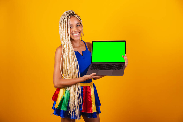 beautiful black, brazilian woman with braids, wearing clothes for carnival. Holding notebook. showing green screen of chroma. - Fotó, kép