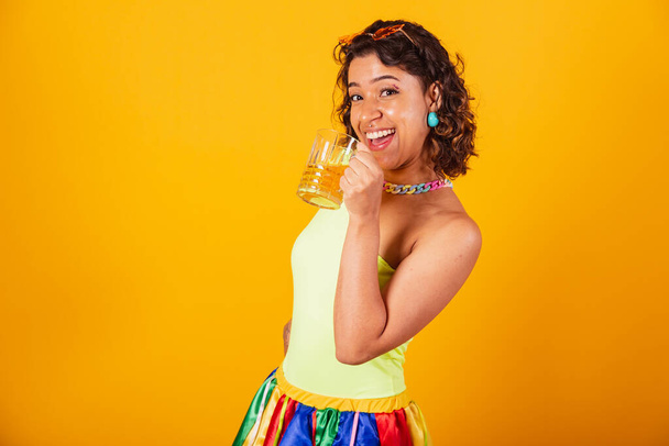 belle fille brésilienne afro-américaine en vêtements de carnaval tenant un verre de bière. boire de la bière et s'amuser. - Photo, image