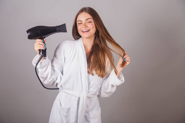 Brazilian blonde woman showing wonderful hair. dressed in a robe. using hair dryer. - 写真・画像